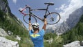 CLOSE UP: Unrecognizable fit biker stands at the side of road hoisting his bike.