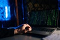 Close-up of unrecognizable hacker engaged in hacking into security system on laptop green binary code on screen with