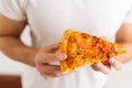 Close-up of unrecognizable man wearing white clothes holding in hands piece of appetizing pizza on white isolated