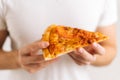 Close-up of unrecognizable man wearing white t-chirt holding in hands piece of appetizing pizza on white isolated