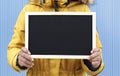 Close up of unrecognizable person holding a blank chalkboard. Blue background