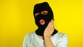 Close up of unrecognizable woman in black balaclava stroking her head and face on yellow background. Unknown person