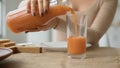 Close up unrecognizable woman pour orange juice from jar to glass on kitchen table. Female hands pouring fresh drink Royalty Free Stock Photo