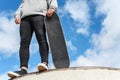 Close up of unrecognizable young man holding skateboard in the park on blue sky background. Royalty Free Stock Photo