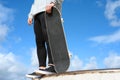 Close up of unrecognizable young man holding skateboard in the park on blue sky background. Royalty Free Stock Photo