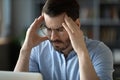 Unwell young man suffering from headache at workplace