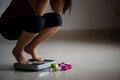 Close up upset female leg stepping on weigh scales with measuring tape, pink dumbbell and green apple. Healthy lifestyle, food and