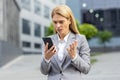 Close-up of upset senior business woman holding phone, female worker in business suit receiving bad accusations online