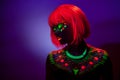 Close up UV portrait of a girl with artistic colorful makeup and orange wig, with closed eyes, violet background. Royalty Free Stock Photo