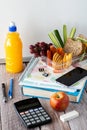 Close up of a variety of school supplies with a lunch kit on top and bottle of juice to the side, against a whiteboard. Royalty Free Stock Photo