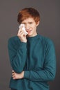 Close up vertical portrait of dramatical ginger good-looking teenager in green sweater holding napkin in hand, wipes up Royalty Free Stock Photo