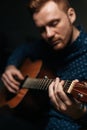 Close-up vertical portrait of guitarist singer male playing acoustic guitar sitting on armchair in dark living room. Royalty Free Stock Photo