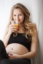 Close up vertical portrait of young good-looking light-haired pregnant mother with wavy hair sitting on window sill in Royalty Free Stock Photo