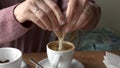 Woman tearing open brown sugar stick, sweetening a cup of her espresso coffee