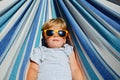 Calm little blond boy with sunglasses rest in hammock