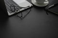 Close-up view from above of laptop, glasses with notebook and cup coffee. Workplace office with dark grey desk. Royalty Free Stock Photo