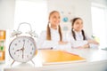 Close-up view of alarm clock two person nice attractive smart clever diligent cheerful cheery girls sitting still in Royalty Free Stock Photo