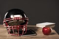 close up view of american football helmet, textbook, apple and stack of books