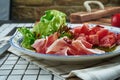 Close up view on appetizing salad with parma ham, lettuce, pesto sauce and marinated tomatoes in beautiful blue ceramic plate on Royalty Free Stock Photo