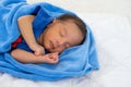 Close up view of Asian young newborn baby is sleeping with blue towel on white bed in the bedroom with soft light Royalty Free Stock Photo