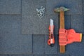 Close up view on asphalt shingles on a roof with hammer,nails and knife. Use of gloves in construction.