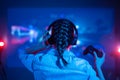 Close-up view from back of emotional gamer woman playing video game at home in front of big screen with headphone and joystick.