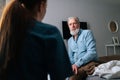 Close-up view from back of female doctor talking to sick senior male patient sitting on bed at nursing home. Royalty Free Stock Photo