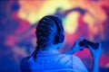 Close-up view from back of gamer woman playing video game at home in front of big screen with joystick and headphone. Colorful