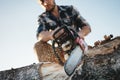 Close up view on bearded strong lumberjack wearing plaid shirt sawing tree with chainsaw for work on sawmill Royalty Free Stock Photo