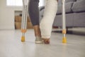 Close up of a woman's leg with a broken leg in a cast walking with crutches in the living room.