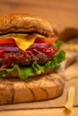 Close-up view of big tasty burger with beef, tomato, lettuce, red onion, cheese, mustard and ketchup on wooden chopped board with Royalty Free Stock Photo