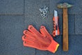 Close up view on bitumen asphalt shingles on a roof with hammer,nails and stationery knife. Use of gloves in construction. Royalty Free Stock Photo