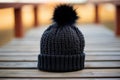 A close up view of a black crocheted beanie with a faux fur pompom.