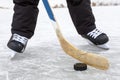 Close-up view at black puck and hockey skates on lake ice, teenage male legs, front view