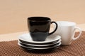 Close up view of black tea cup on the stack of the white and black plates near white tea cup on tablemat.