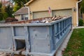 Closeup view of a blue dumpster filled with construction debris in the driveway of a yellow house in front of the garage doors Royalty Free Stock Photo