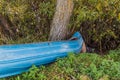 Close-up view of blue rowing metal boat parked on shore of river in bushes.