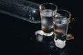 Close-up view of bottle and glasses of vodka standing isolated on black.