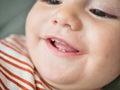 A close-up view capturing the joyful expression of a baby who is smiling and showing two little teeth. The childs eyes