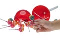 Close-up view of child\'s hand holding ?hupa ?hups lollipops on background of unscrewed plastic box of lollipops