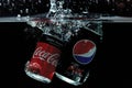 Close up view of coca and pepsi falling in water on black background.