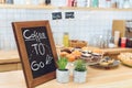 close-up view of coffee to go inscription on board, green plants and various pastries on counter