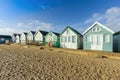 A close up view of colorful beach huts with a sandy beach in the foreground under a majestic blue sky and some white clouds Royalty Free Stock Photo