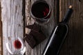 Close-up view of composition with dark chocolate, elegant bottle and glass with remains of red wine on rustic wooden background. Royalty Free Stock Photo