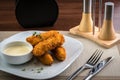 Close up view of crispy deep fried fish fingers with breadcrumbs served with sauce. Salt and Pepper shakers on the wooden table Royalty Free Stock Photo