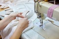 Close up view of cropped female hands sewing white fabric on professional manufacturing machine