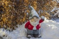 Close up view of cute figure of gnome standing in snow covered garden on frosty winter day.