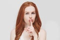 Close up view of cute ginger young woman, holding a finger on her lips, saying `shh`, asking to keep silent about bi Royalty Free Stock Photo