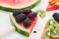 Close up view of delicious dessert with watermelon on sticks, kiwi and blackberries on white background.