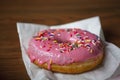 Close up view of a Delicious Pink donut with colorful sprinkles sitting on a table at a coffee shop
